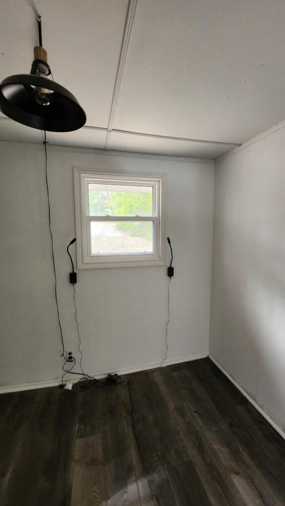 Finished basement room with painted walls, dark plank flooring and a pendant light