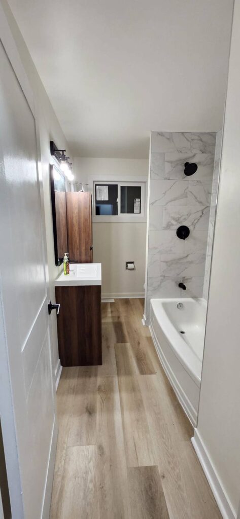 Renovated bathroom with marble-look tile tub surround, walnut vanity and black fixtures
