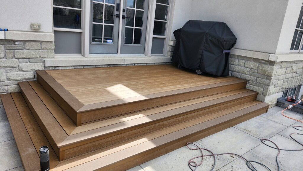 New composite deck with wide steps beside a stone-clad home