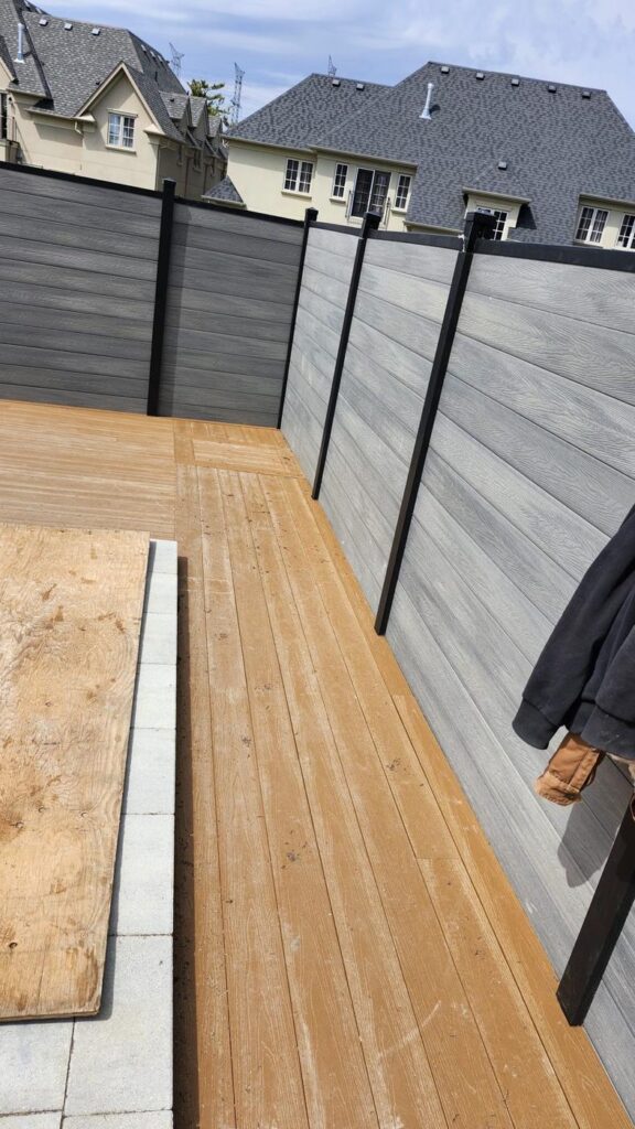 Deck boards installed beside a grey composite privacy fence