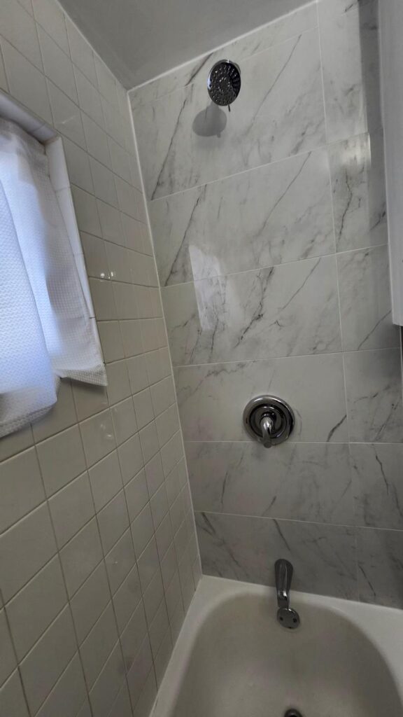 Marble-look tile shower wall with tub and chrome fixtures